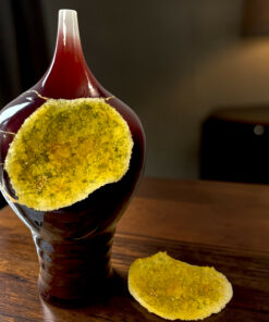 Close-up of a dark red glass bottle with a bright yellow sugar crust around its neck on a wooden table.