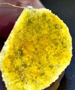 Close-up of a yellow druzy quartz geode with sparkling crystals along the edge, placed beside a pink glass vessel.