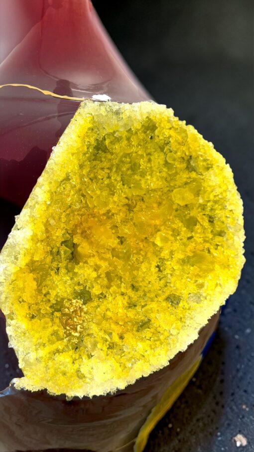 IMG_0787 2 | Kintsugi by Myriam GREFF Close-up of a yellow druzy quartz geode with sparkling crystals along the edge, placed beside a pink glass vessel.