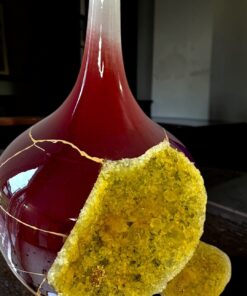 Close-up of a red glass bottle with a frosted neck and a yellow crystalline crust on one side.