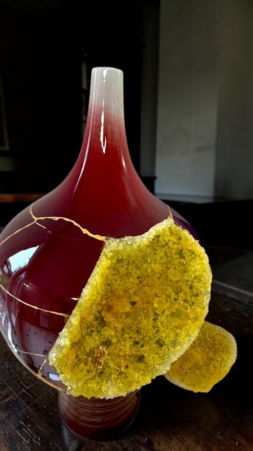 IMG_0790 2 | Kintsugi by Myriam GREFF Close-up of a red glass bottle with a frosted neck and a yellow crystalline crust on one side.