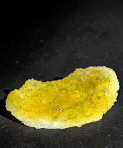 Yellow crystalline rock fragment resting on a black surface, with sparkly, uneven crystals.