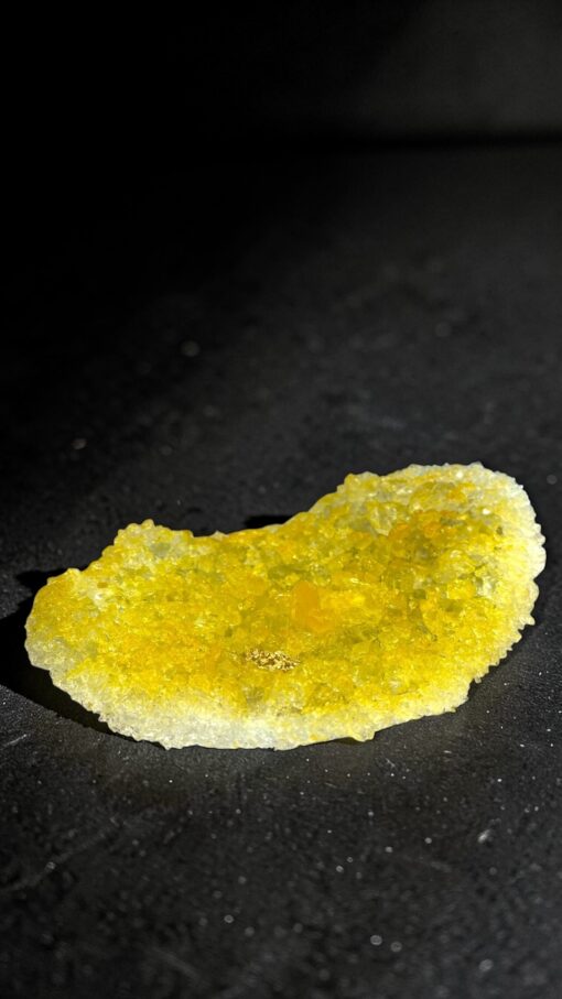 IMG_0795 2 | Kintsugi by Myriam GREFF Yellow crystalline rock fragment resting on a black surface, with sparkly, uneven crystals.