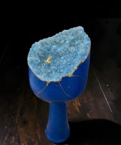 Blue goblet topped with a rough blue geode cluster showing gold flecks against a dark background.