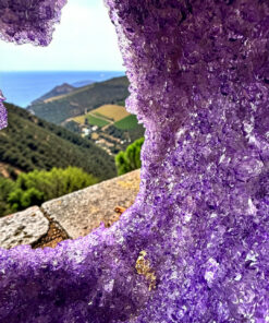 Close-up of purple amethyst crystals forming a cave opening, with a valley and sea visible beyond the opening.