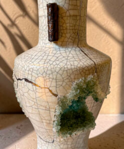 Cream crackled-glaze ceramic vase with a dark brown neck ornament and a green mineral crystal cluster on its side.