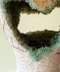 Cracked ceramic bust with a jagged teal glass necklace around the neck, resembling broken shards.