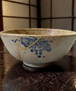 Close-up of a white ceramic bowl with blue underglaze design and a yellow string draped over its rim on a dark wooden table surface.