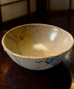 Close-up of a light ceramic bowl with gold kintsugi repairs on a dark wooden table