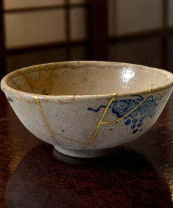 Close-up of a ceramic bowl with blue glaze designs and gold streaks on a dark wooden table.