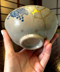 Close-up of a ceramic sphere with blue floral pattern and gold decorative crackle held in hands