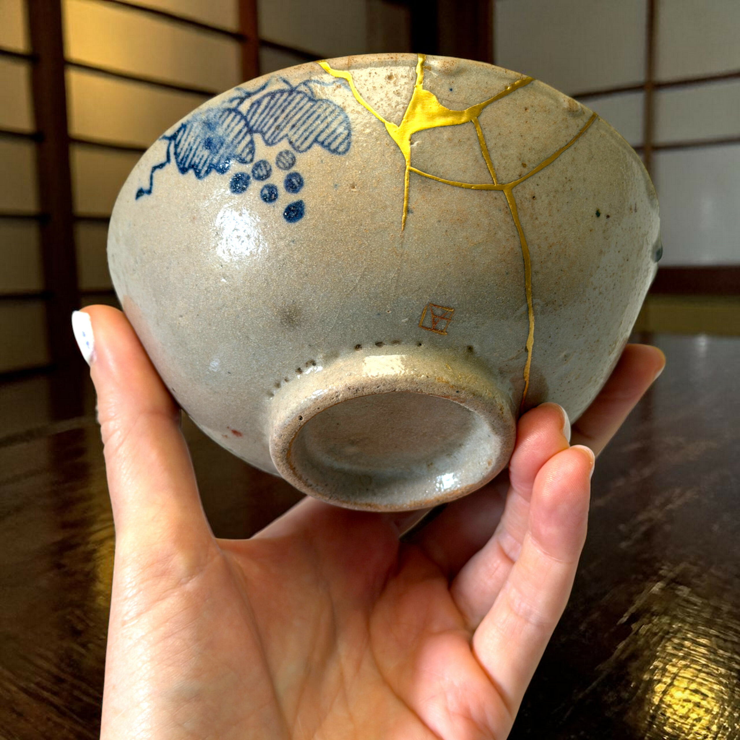 IMG_1582-Photoroom | Kintsugi by Myriam GREFF Close-up of a ceramic sphere with blue floral pattern and gold decorative crackle held in hands
