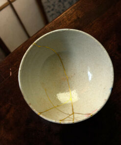 Partial view of a pale ceramic plate with thin gold thread decorations laid on a dark wooden table surface.