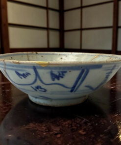 Close-up of a blue-and-white ceramic bowl resting on a dark wooden table with a lattice screen in the background.