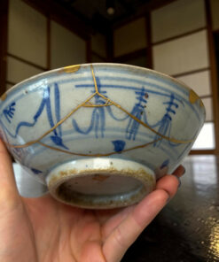 Close-up of a blue and white ceramic bowl held by hands, with a gold string wrapped around it.