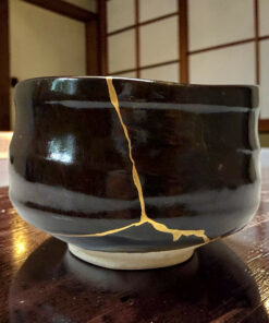 Close-up of a glossy black ceramic mug with a yellow hairline crack running vertically down its side on a wooden table.