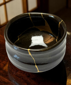 Close-up of a black ceramic vessel with gold repair lines (kintsugi) on a wooden table.