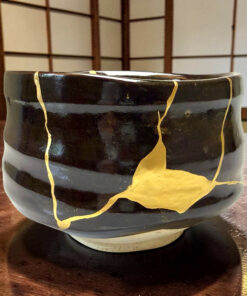 Close-up of a black ceramic pot with irregular gold ribbon-like decorations on its surface.