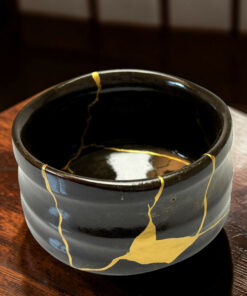 Black ceramic pot wrapped with gold ribbon resting on a wooden table