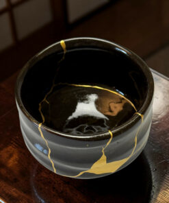 Close-up of a black container with gold paint drips along the rim on a dark wooden surface.