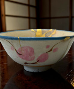 Ceramic bowl with pink flower pattern rests on a dark polished wooden table, close-up view with soft background.