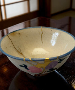 Close-up of a light-colored ceramic bowl with a blue rim on a dark glossy wooden table, showing glaze drips.