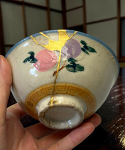 Close-up of a ceramic plate with gold kintsugi repair held in a person's hand.