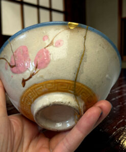 Close-up of a cracked ceramic sphere with gold repair seams, held in a person's hand.