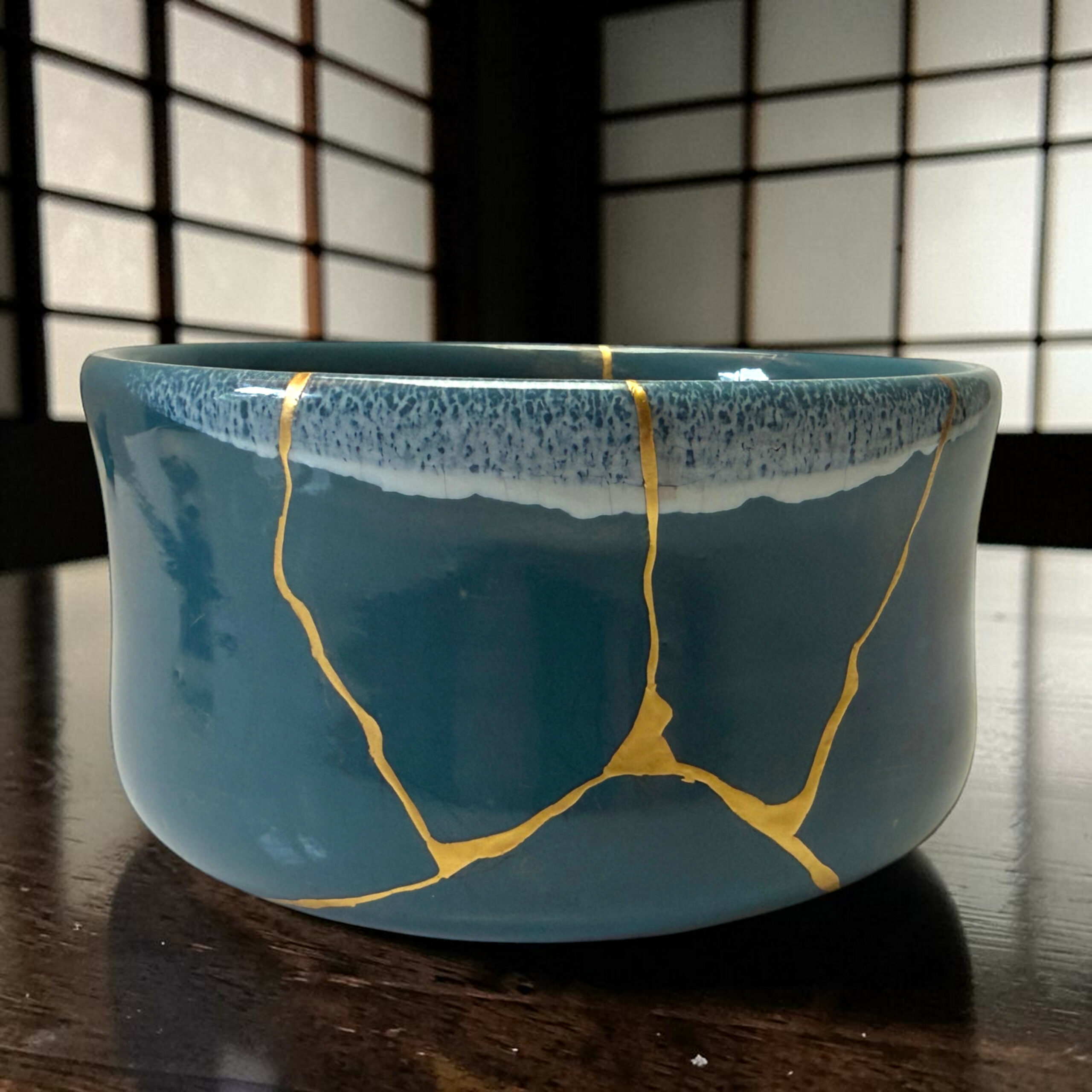 IMG_1675-Photoroom | Kintsugi by Myriam GREFF Blue ceramic bowl with gold streaks on a dark wooden table, background out of focus.
