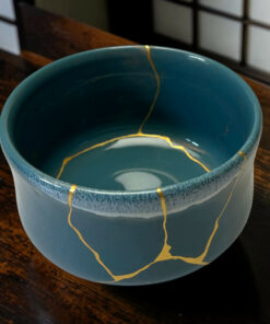 Close-up of a blue ceramic mug with gold glaze marks running along its rim, set on a wooden surface.