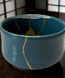 Close-up of a blue ceramic mug on a dark wooden table, with a thin yellow string running along the rim and down the side.
