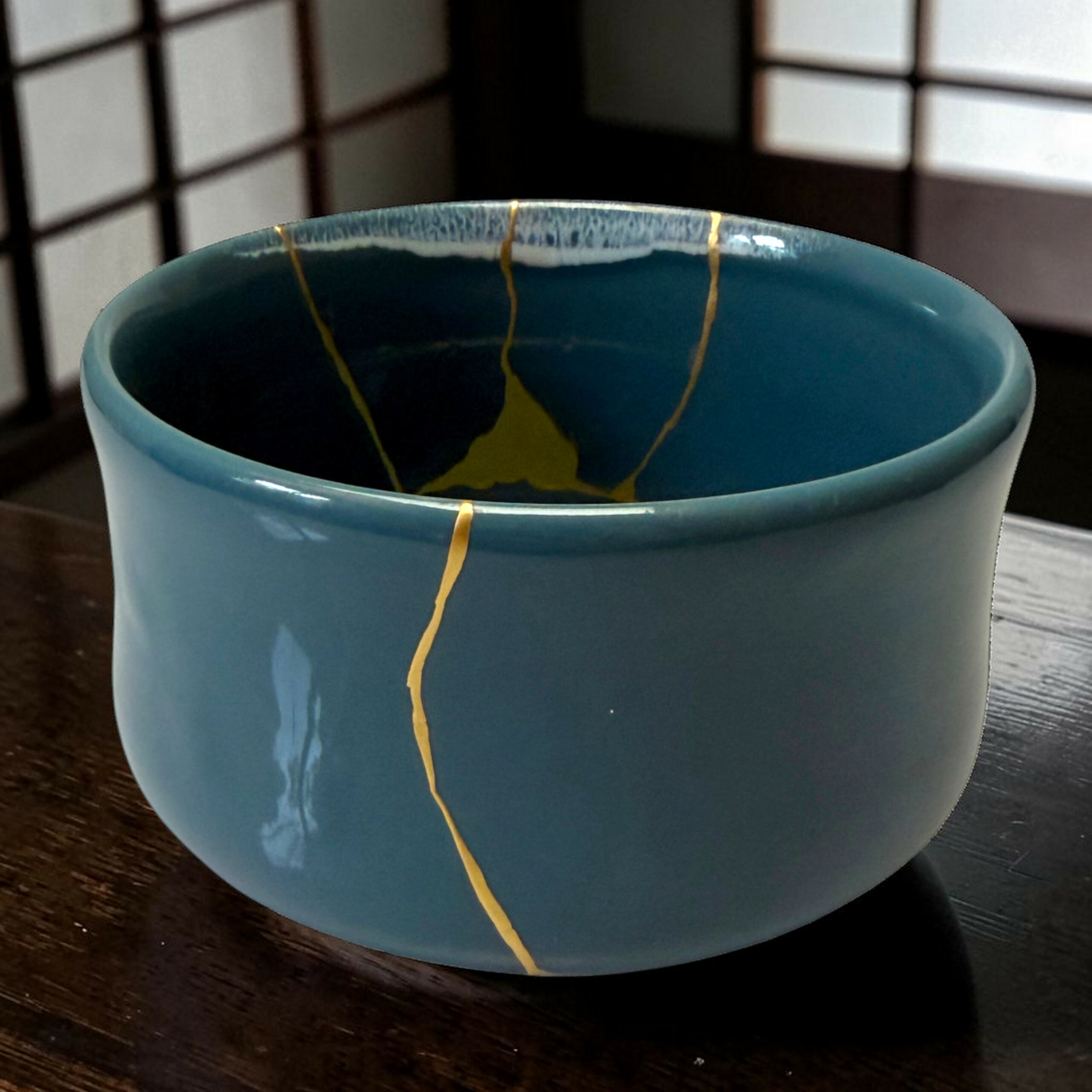 IMG_1677-Photoroom | Kintsugi by Myriam GREFF Close-up of a blue ceramic mug on a dark wooden table, with a thin yellow string running along the rim and down the side.