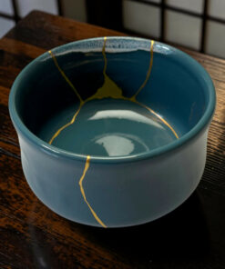 Close-up of a teal ceramic mug with yellow crackle glaze along the rim, placed on a dark wooden table.