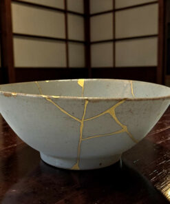 Blue ceramic bowl on a dark wooden table with gold tape-like seams showing repair lines (kintsugi).