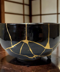 Close-up of a glossy black ceramic mug or cup with irregular gold crackle lines, resting on a dark wooden table.