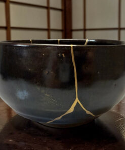 Close-up of a dark ceramic pot with a thin yellow string draped over its rim, with a wooden lattice wall in the background.