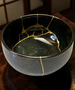 Close-up of a black ceramic bowl with gold lacquer cracks along the rim, resting on a wooden table.