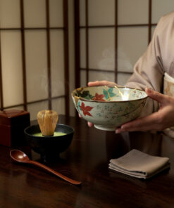 Person in a kimono holds a decorated ceramic tea bowl in a traditional Japanese tea ceremony, with steam rising.**