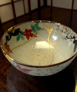 Close-up of a decorative ceramic plate with gold flecks and colorful floral pattern on a dark wooden surface (crackle glaze visible).