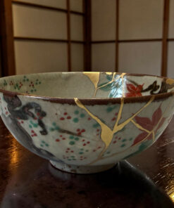 Two decorative ceramic bowls stacked on a dark wooden table, featuring floral patterns and gold lattice accents.