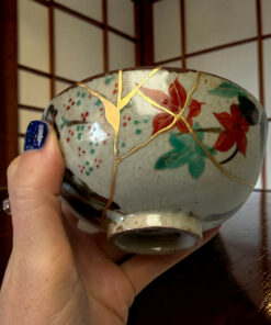 Close-up of a ceramic decorative orb with gold crackle lines and red/green floral patterns, held by a person with blue nail polish.