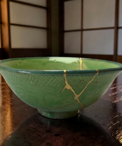 Close-up of a green ceramic bowl with gold crackle lines resting on a dark wooden table.