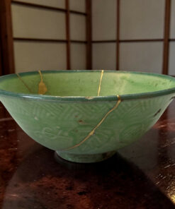 Green ceramic bowl in the foreground with a brown wooden lattice background behind it on a dark wooden surface.