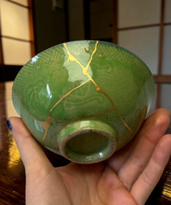 Close-up of a green ceramic vase with gold veining, held in both hands indoors.