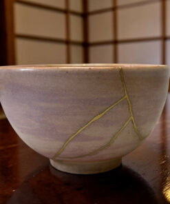 Close-up of a light gray ceramic bowl with a yellow string draped over its rim, resting on a dark wooden table.