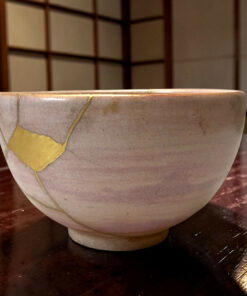 Close-up of a light ceramic pot with yellow tape on its side, resting on a dark wooden table.