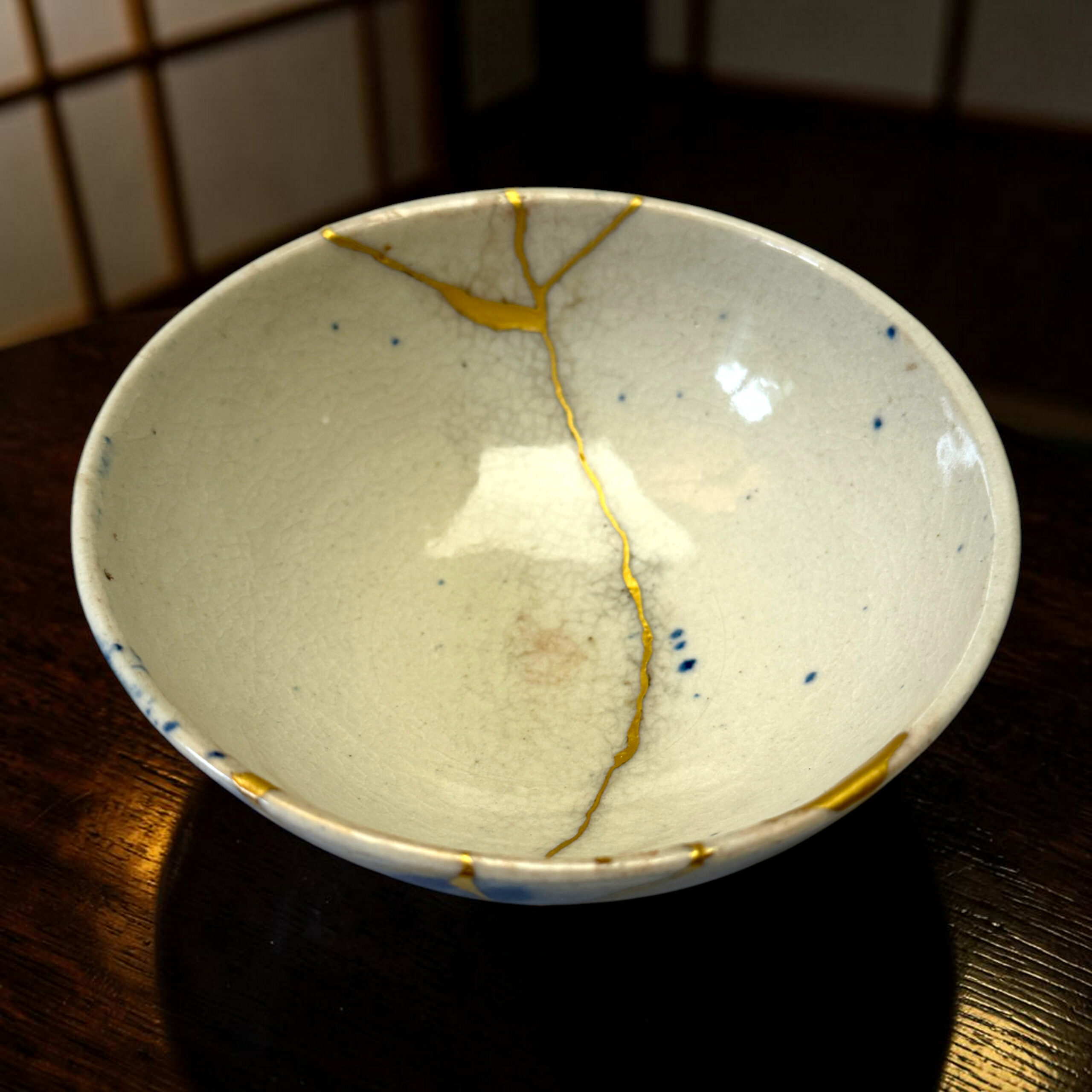 IMG_1711-Photoroom | Kintsugi by Myriam GREFF Close-up of a light ceramic bowl with yellow drizzle glaze, positioned on a dark wooden table.