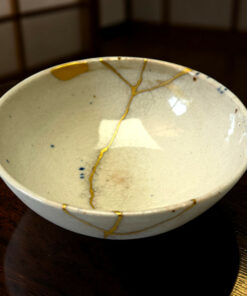 Close-up of a ceramic bowl with gold repair lines (kintsugi) on a dark wooden table.
