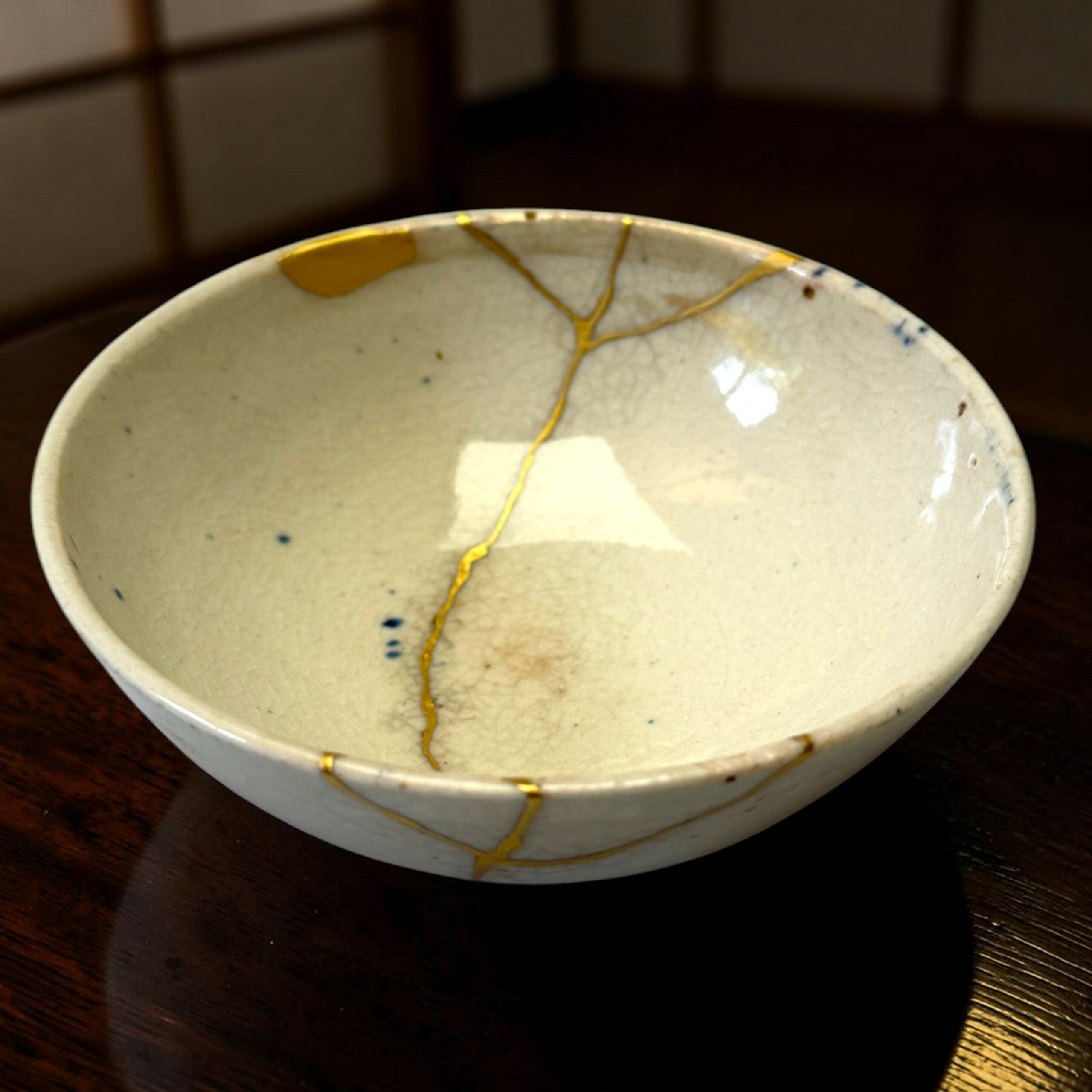 IMG_1714-Photoroom | Kintsugi by Myriam GREFF Close-up of a ceramic bowl with gold repair lines (kintsugi) on a dark wooden table.