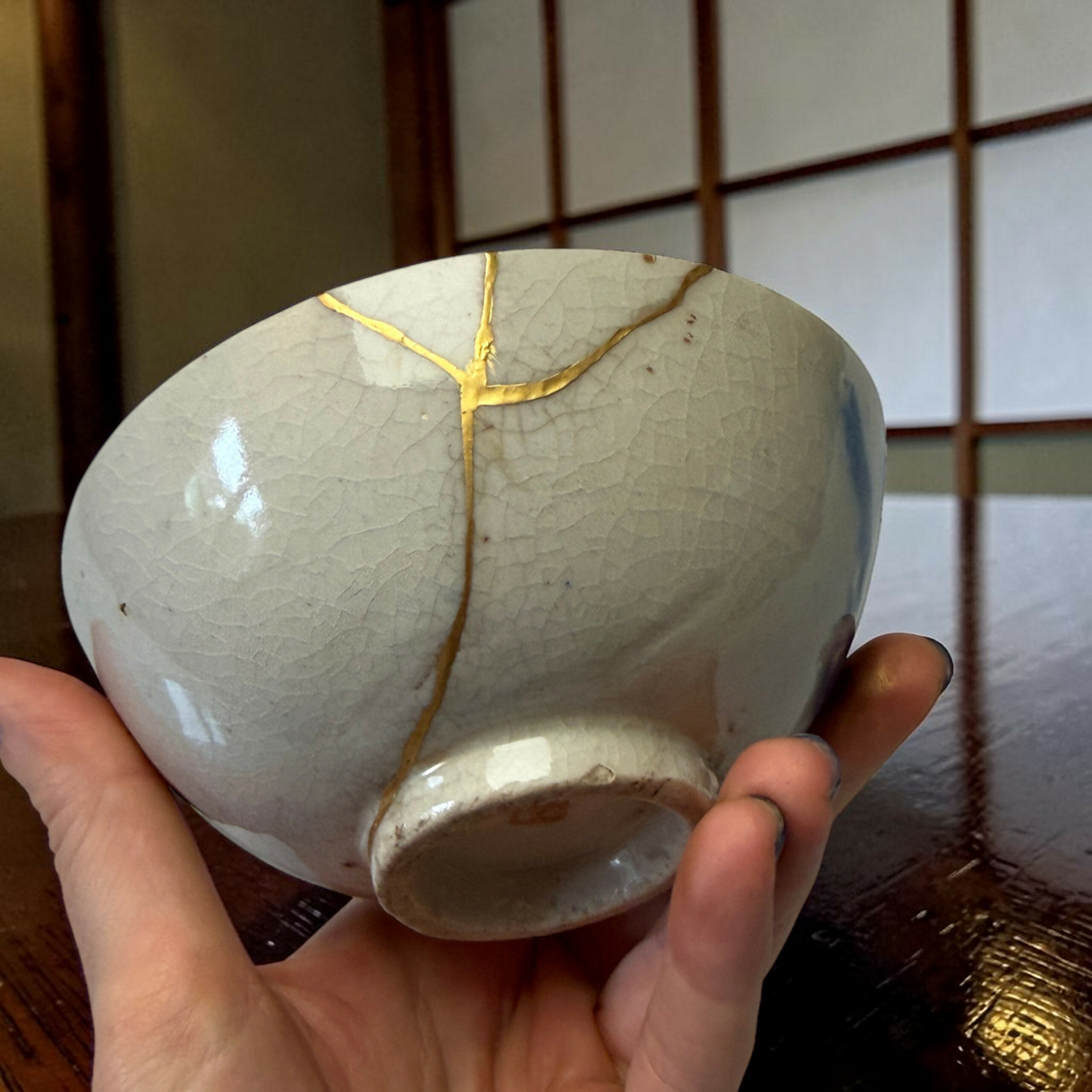 IMG_1717-Photoroom | Kintsugi by Myriam GREFF Hands cradle a large smooth gray ceramic sphere with gold cracks (kintsugi) against a wooden surface.